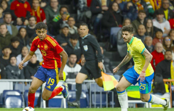 MADRID, 26/03/2024.- El delantero de la selección española Lamine Yamal (i) disputa un balón frente a Lucas Beraldo, defensa de la selección brasileña, durante el partido amistoso que las selecciones nacionales de fútbol de España y Brasil disputan hoy martes en el estadio Santiago Bernabéu, en Madrid. EFE/Mariscal